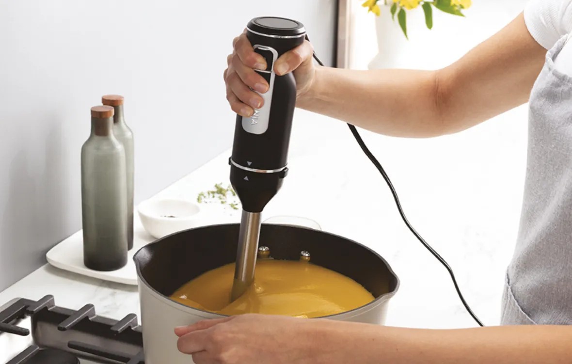 Людина використовує занурювальний блендер Ninja для приготування крем-супу в каструлі.