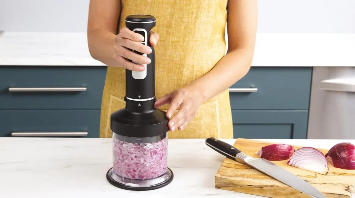 Людина подрібнює червону цибулю в контейнері подрібнювача блендера Ninja на кухонному столі.