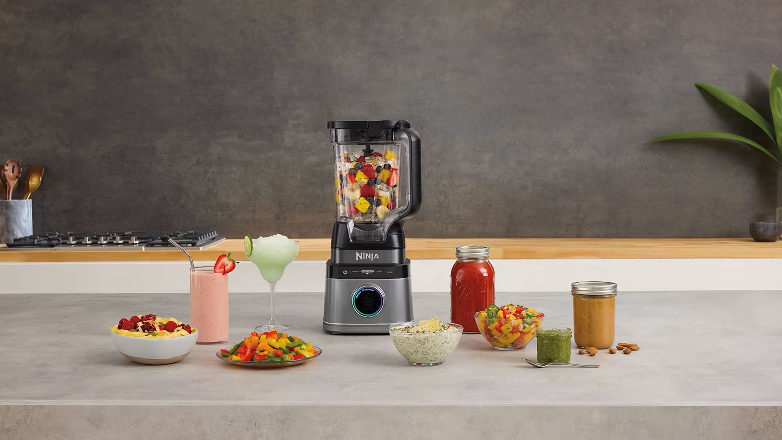 Блендер Ninja із нарізаними фруктами всередині чаші, поруч різні страви та напої — смузі, соуси, пасти
