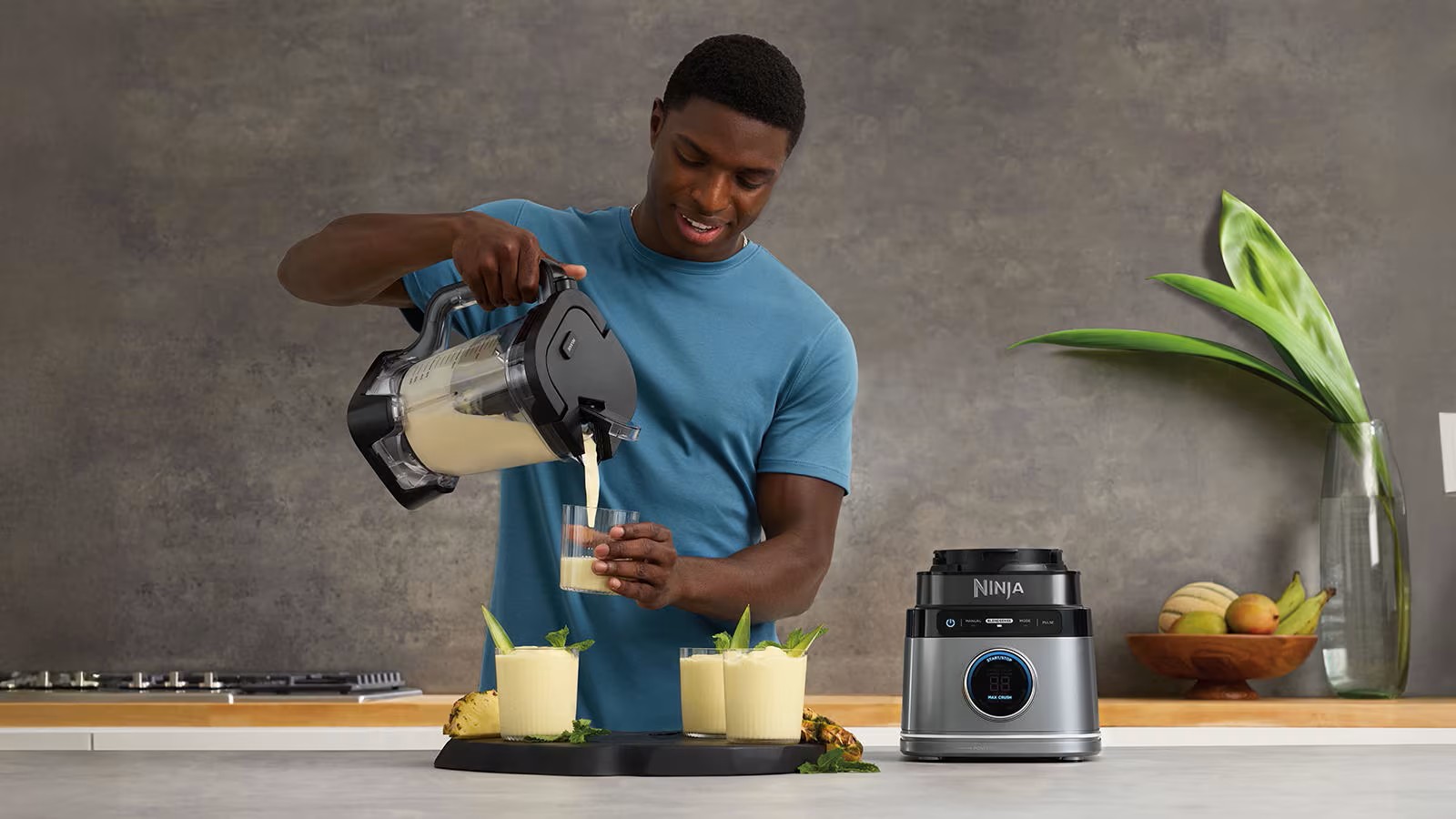 Чоловік наливає напій із блендера Ninja у склянку, поруч стоять готові коктейлі з ананасом