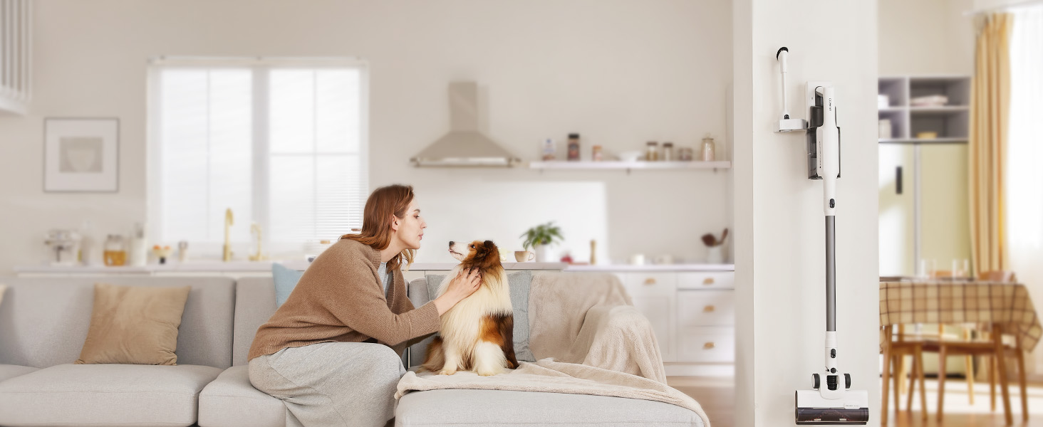 Жінка грається із собакою на дивані, поруч на стіні закріплений бездротовий пилосос Tineco на зарядній базі