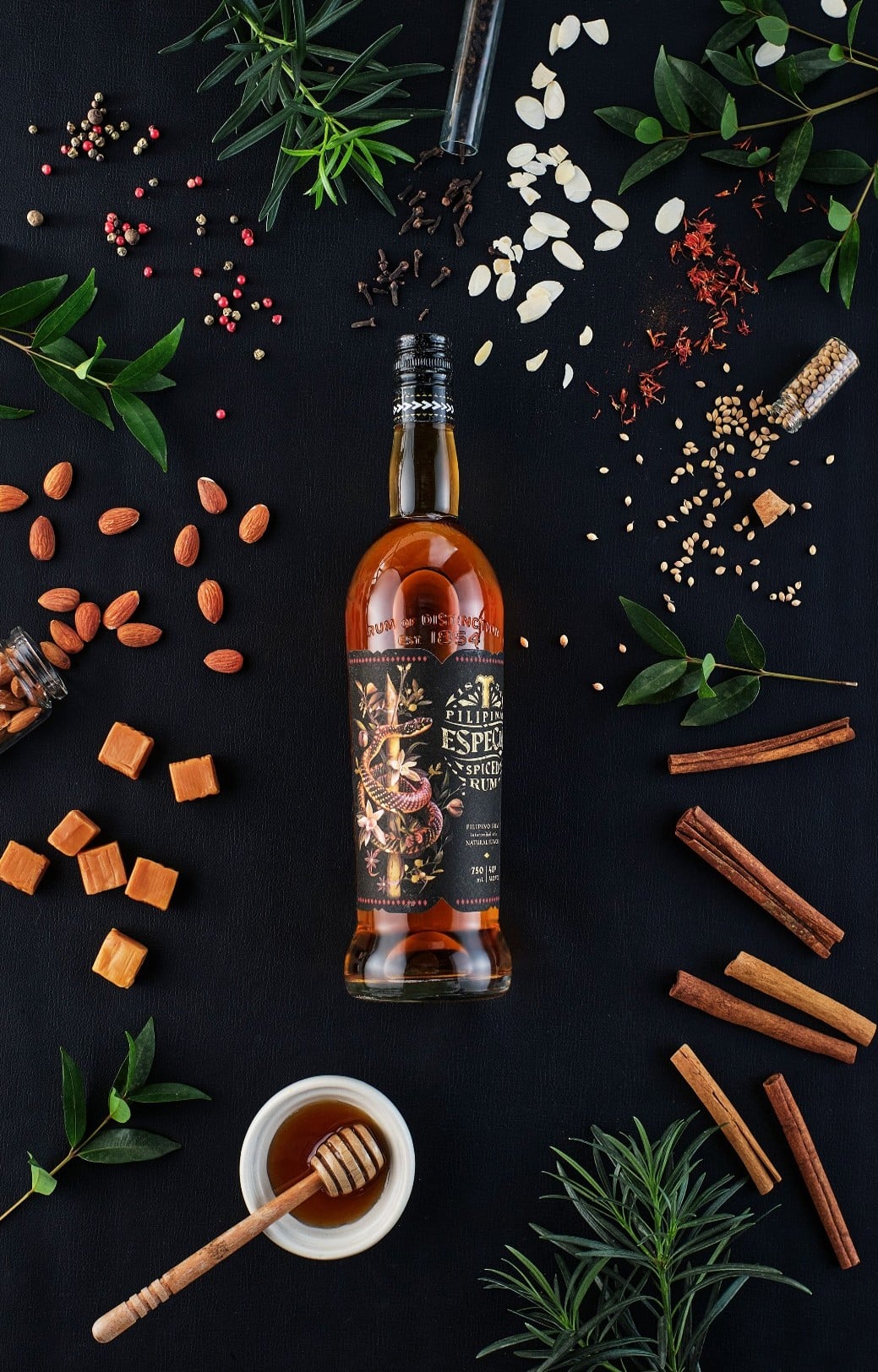 Пляшка рому Especia Spiced Rum серед спецій, горіхів, трав і меду на темному фоні