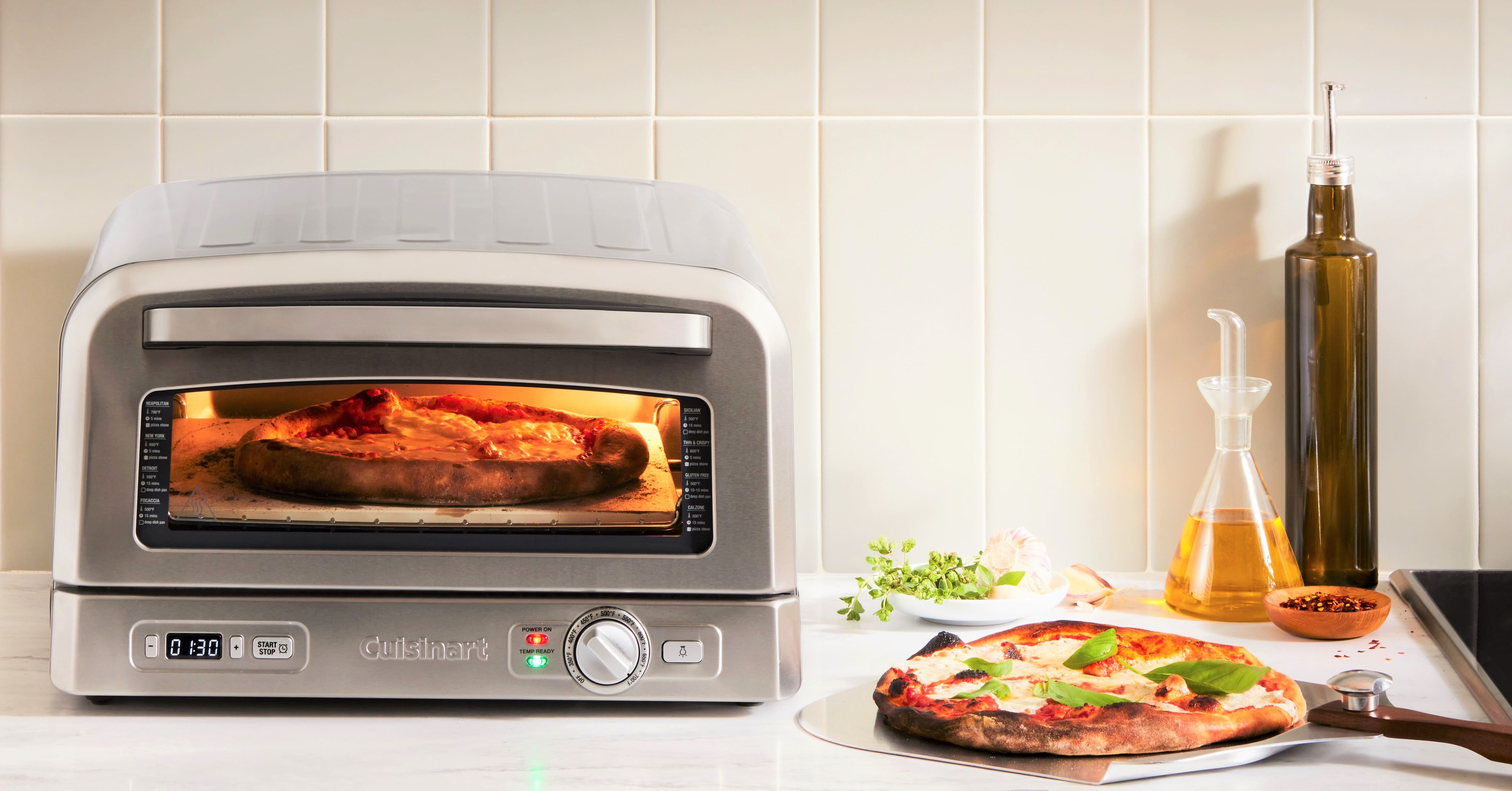 Електрична піч Cuisinart із запеченою піцою всередині на кухонній стільниці, поруч інгредієнти та пляшки з олією