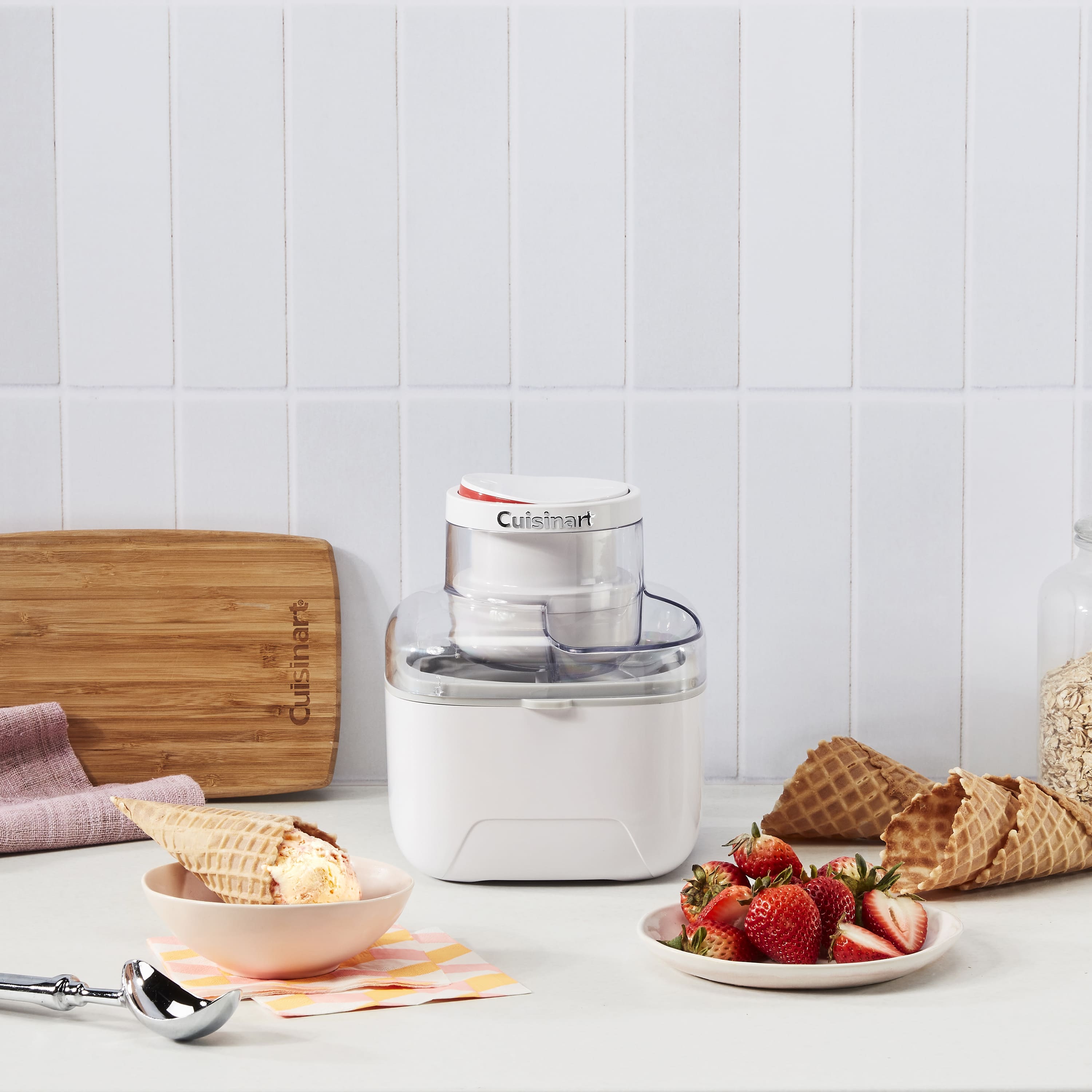 Морозивниця Cuisinart на кухонному столі поруч із вафельними ріжками та полуницею