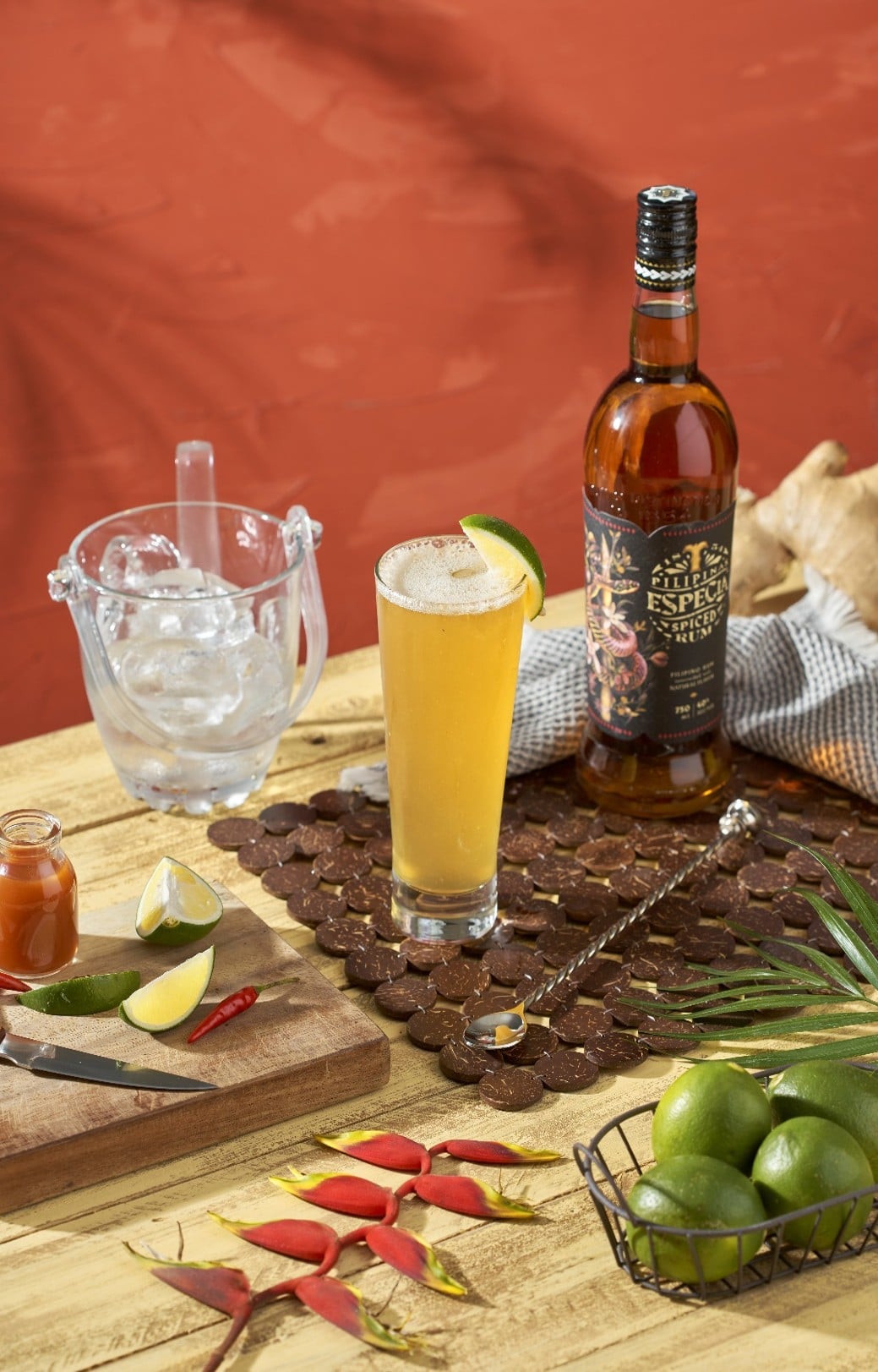 Пляшка рому Especia Spiced Rum поруч із келихом коктейлю, лаймом, льодом і спеціями на дерев’яному столі