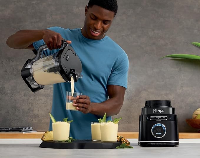 Чоловік наливає напій із блендера Ninja у склянку, приготований коктейль подається на кухні.