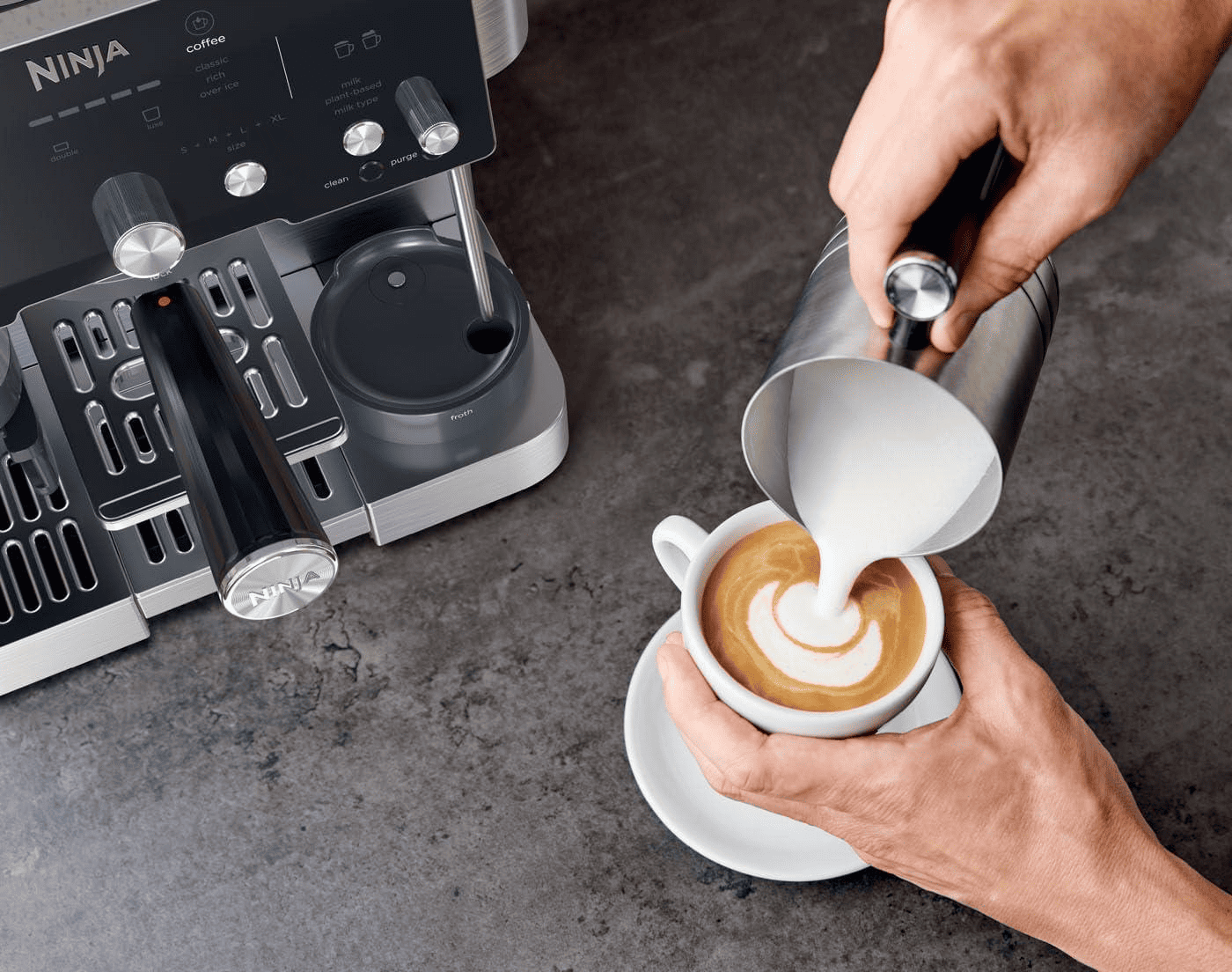 Приготування лате, людина наливає спінене молоко в чашку кави поруч із кавомашиною Ninja